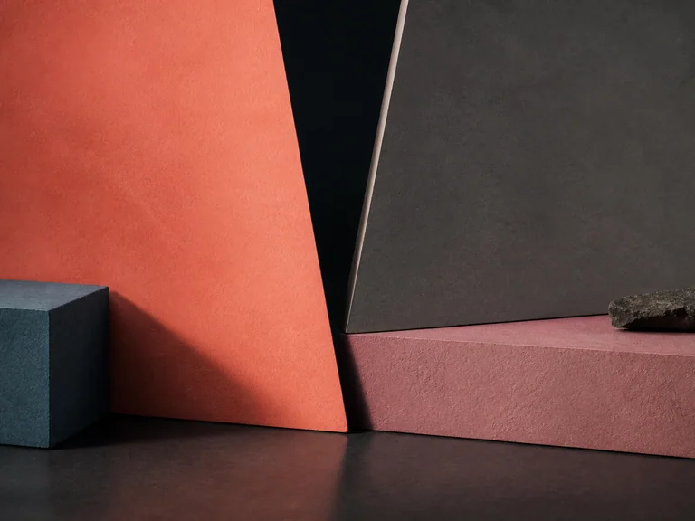 Coral, graphite, rose, and blue-gray angular planes meet at a narrow dark seam with rough stone accents.