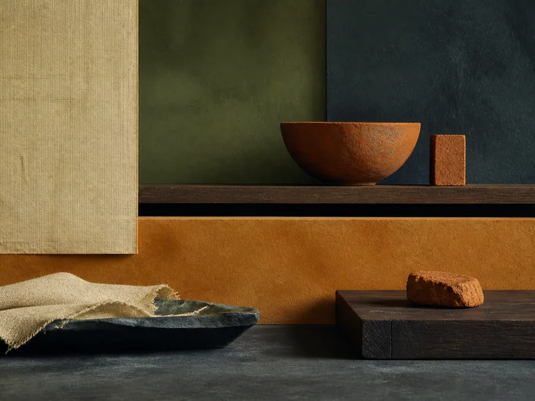 Low linen, terracotta, wood, and slate planes in raw sienna, ivory, olive green, and slate gray.